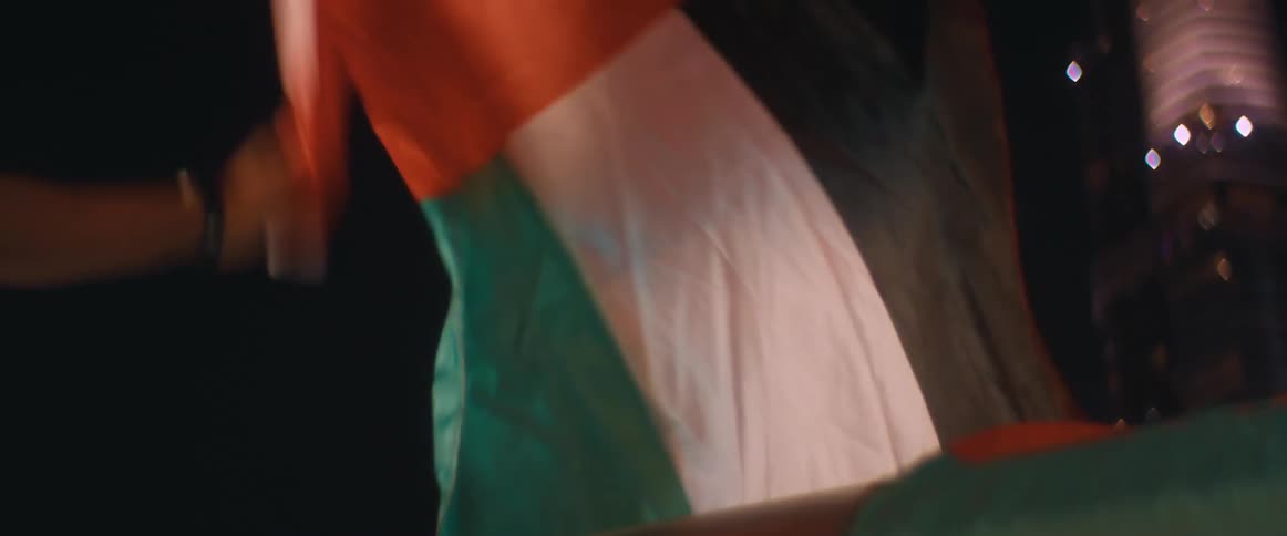 Man shaking and waving a flag from a balcony in the city at night