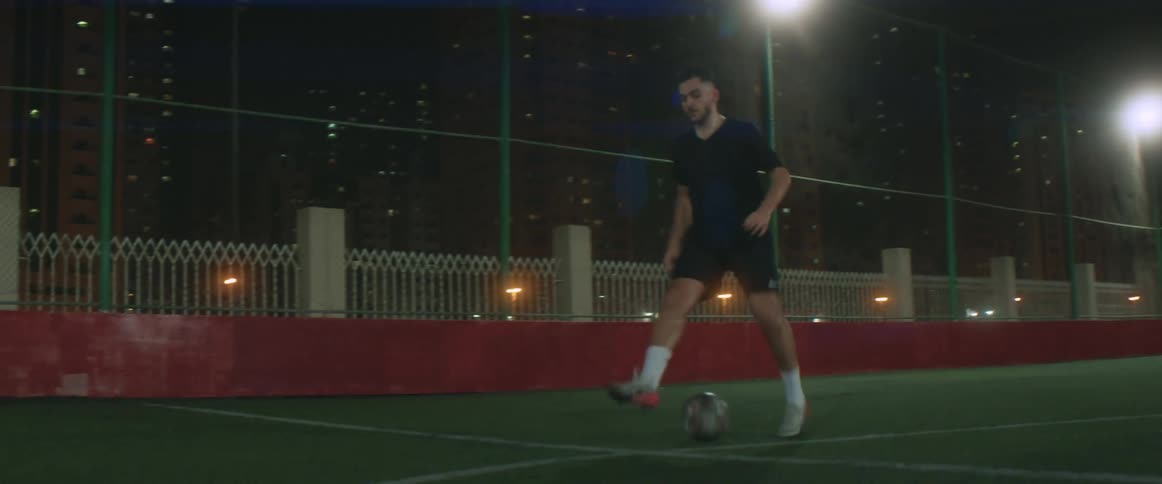 A man is playing soccer on an empty field at night