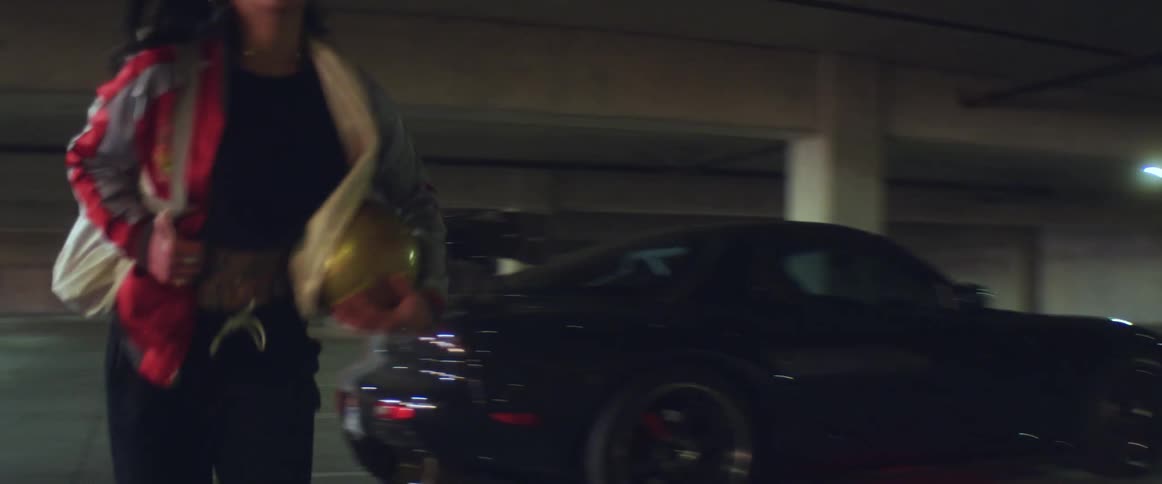 Young woman holding a golden ball runs from a black car parked in a garage