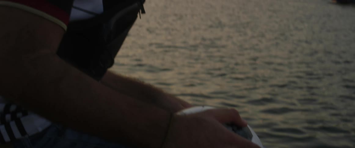 A man holds onto a soccer ball as he stands on a bridge as boats pass by