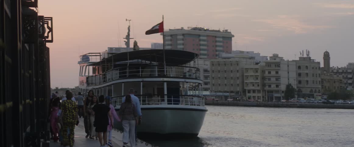 A group of people walk along the water next to a boat docked