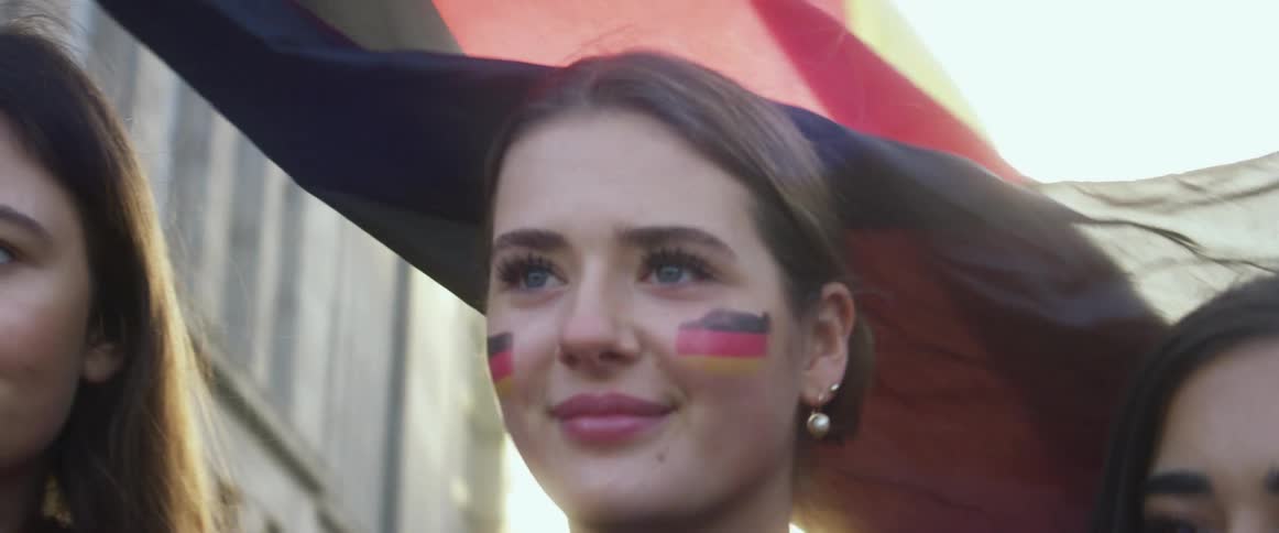 Young group of friends posing in front of a waving germany flag in the city at sunset