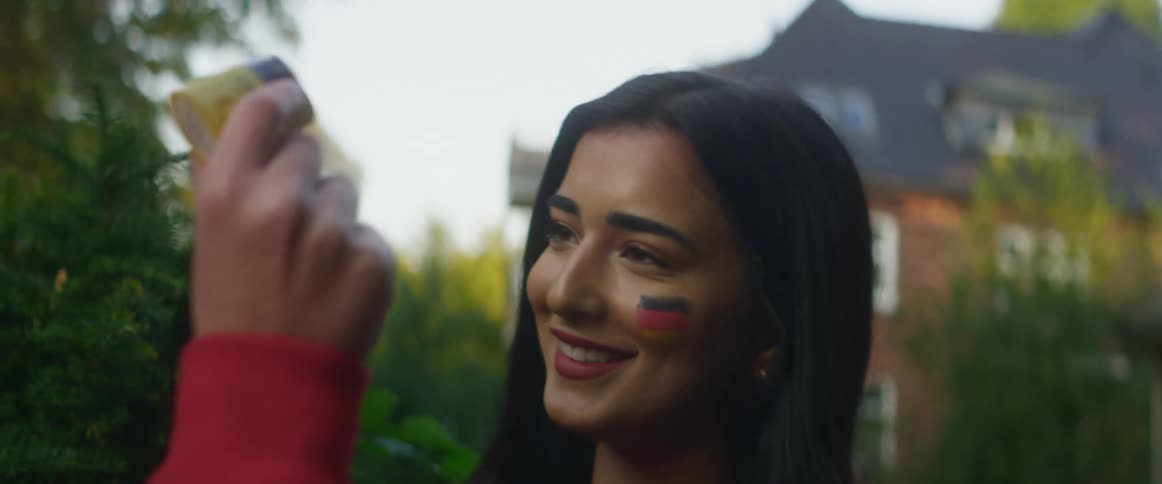 A woman applies soccer fan makeup to her friends face while they are outside