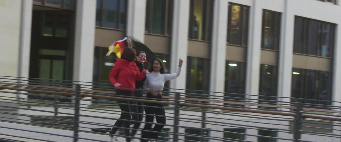 Three friends running with a germany flag over a bridge in the city at evening