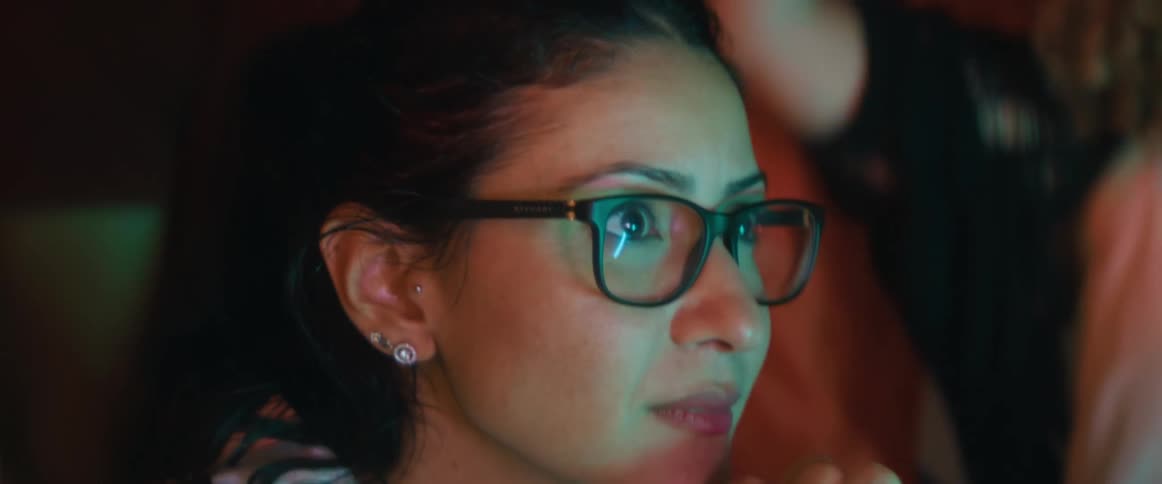 Woman nervously watches screen as others standing behind her cheer
