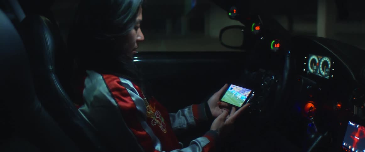 A woman is sitting in her parked car and looking at her cellphone