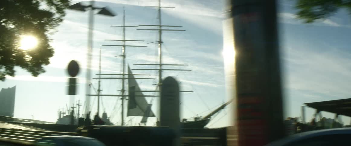 A car driving by ships in a harbor on a sunny day