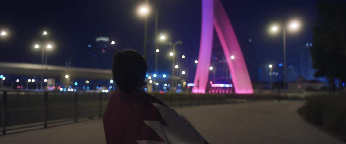 Person stand on walkway near highway on windy night looking toward city buildings
