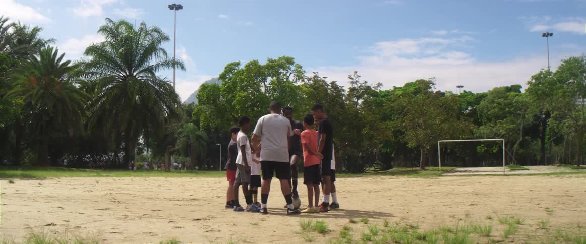 A group of boys stand in a circle on a soccer field and put their hands in the middle as they pick teams