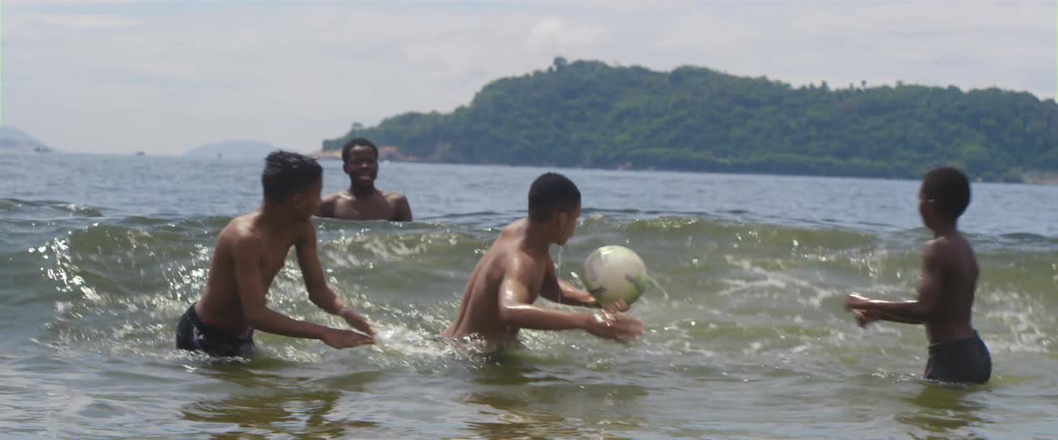 Youths play with ball in ocean near beach