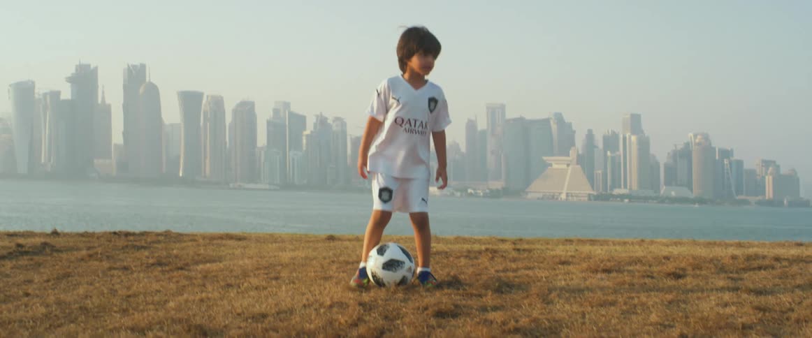 Young boy playing with a soccer ball on the grass near the waterfront city skyline