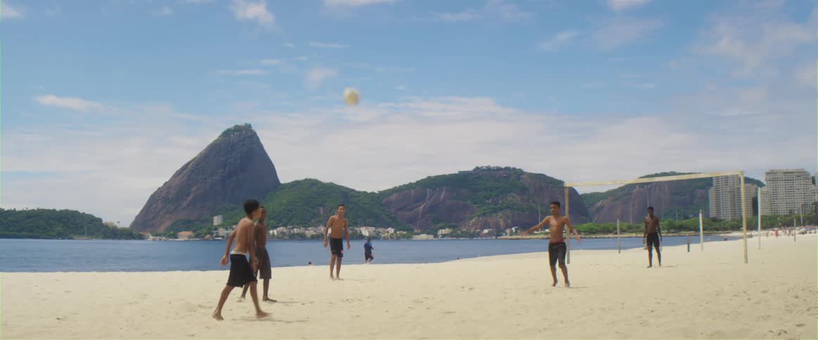 Group of teenagers playing soccer on a beach near pan de azucar mountain in rio de janeiro