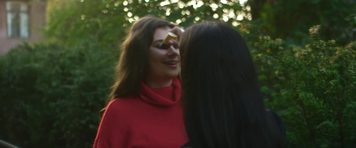 A young woman helps another woman put makeup on her cheek outdoors