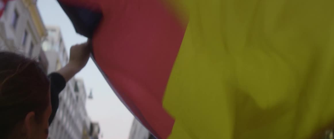 A woman leaning out of the window of a moving vehicle holds out a german flag to allow it to in the wind