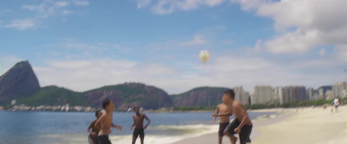 A group of youths plays football on the white sand beach next to sea