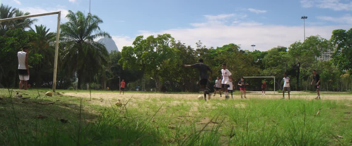 A group of kids plays soccer on a dirt and grass field