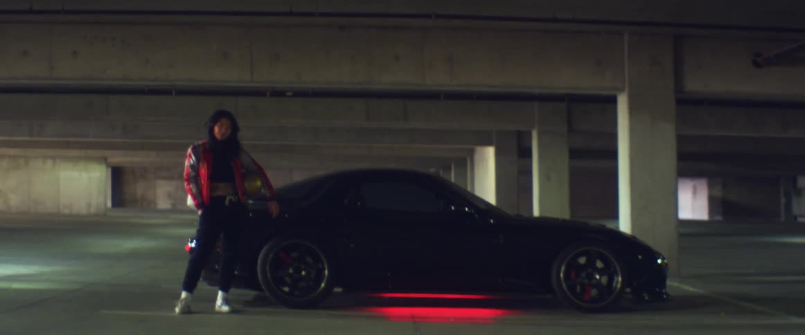 A woman poses next to a sports car in a parking garage
