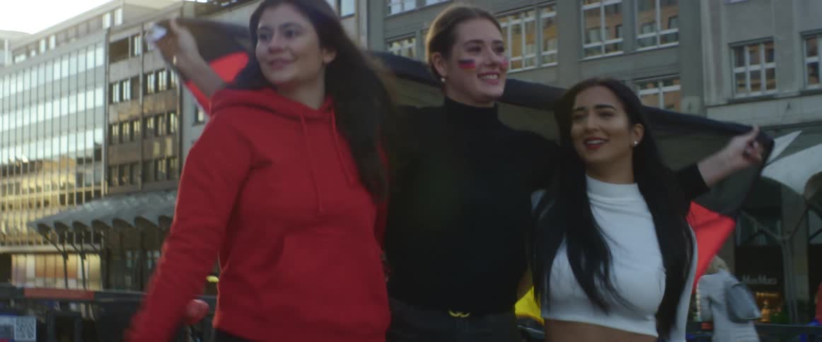 Three friends walk down a street holding a large flag