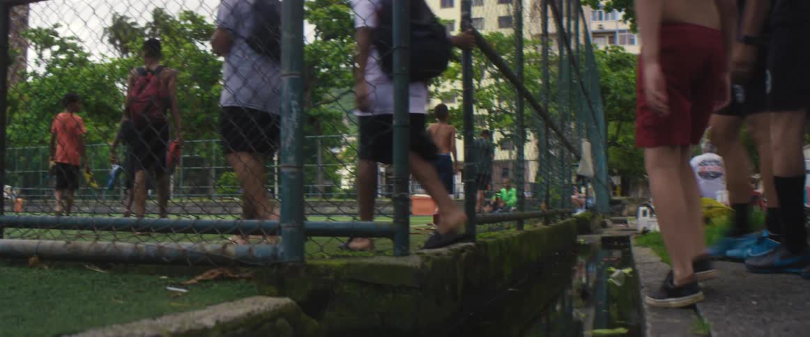 Boys climb over a moat to enter a park while carrying a soccer ball
