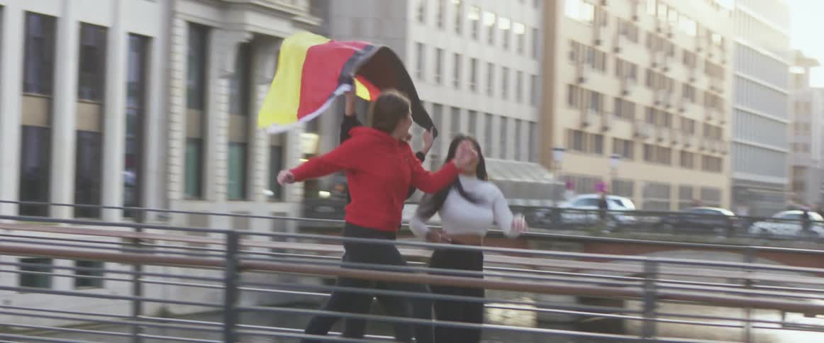 Three teenage girls smiling while running with a flag in an urban setting