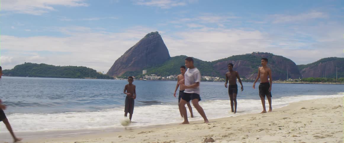 A group of youths plays football on the white sand beach next to the sea