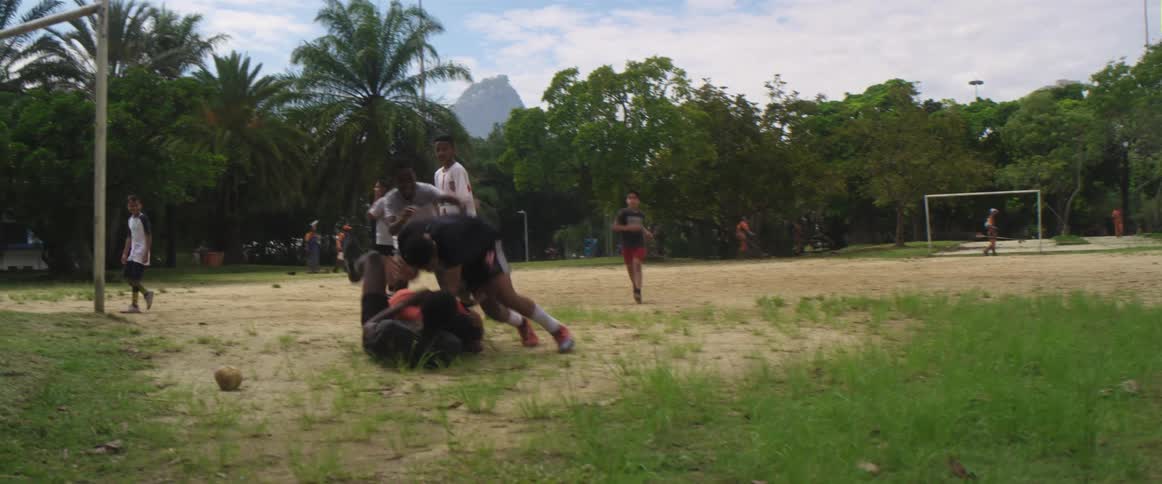 A soccer team celebrates in a heap on the ground as a teammate kicks a ball through the goal