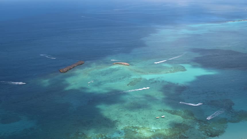 Boats sailing around an island on blue and turquoise ocean water in the daytime