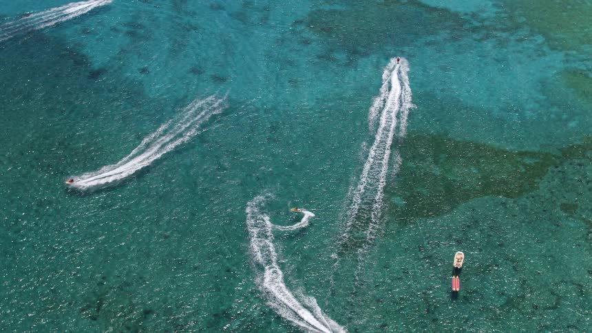 People ride jet skis across azure water leaving wakes