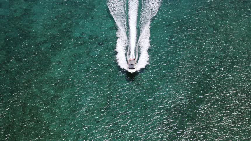 An aerial view of a boat floating over blue and turquoise ocean water