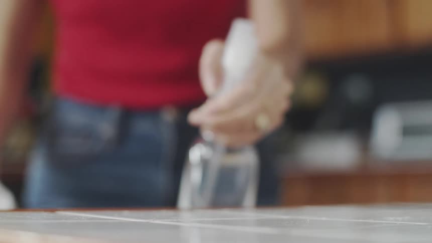 A woman is cleaning a table inside her house during the day
