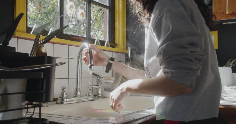 A woman is washing dishes in her house during the daytime
