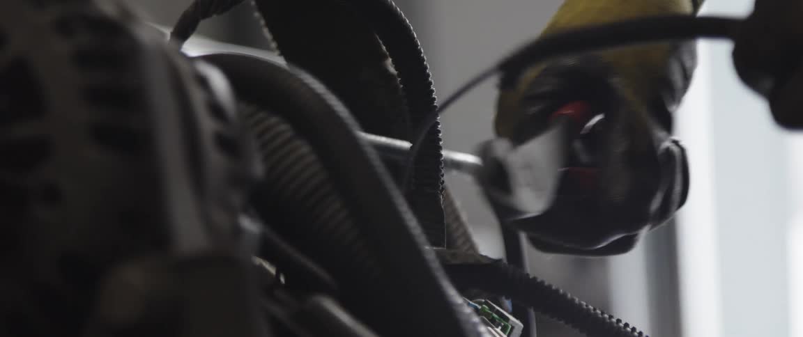 A gloved hand cutting a wire next to black hoses