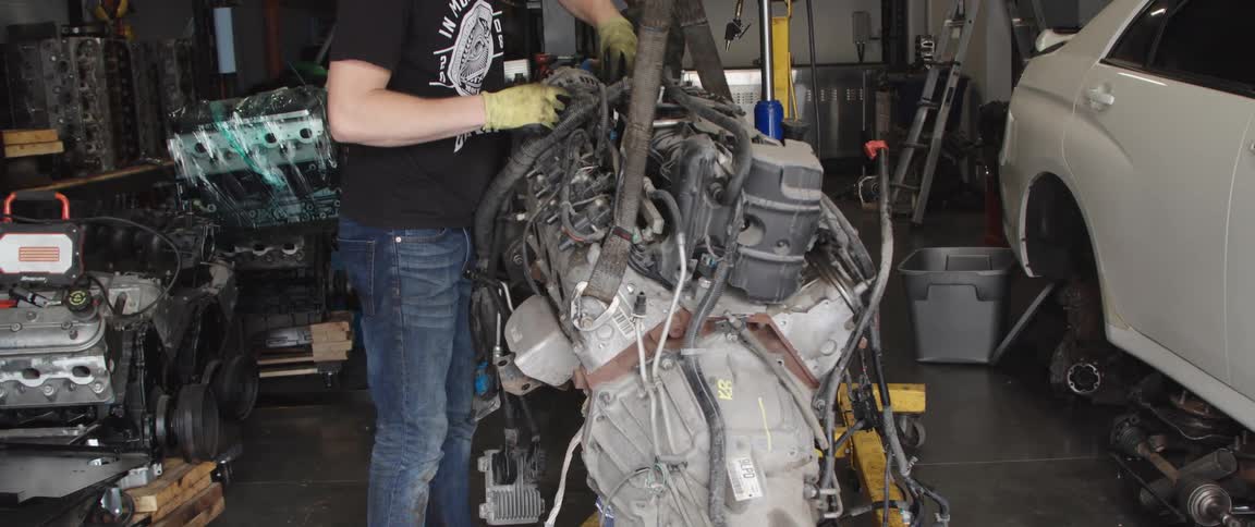 Mechanic working on a big engine suspended from the ceiling inside an auto shop