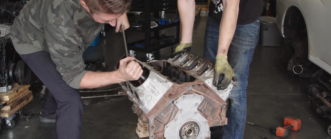 A man is using a wrench on a motor while another one holds the engine block