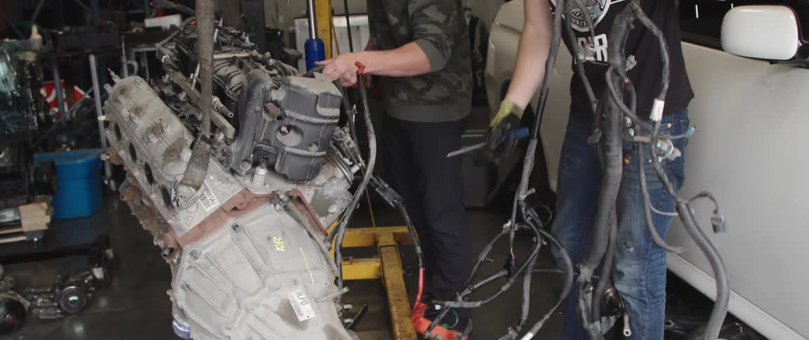 Two men in a shop unravel hoses and look at a piece of equipment