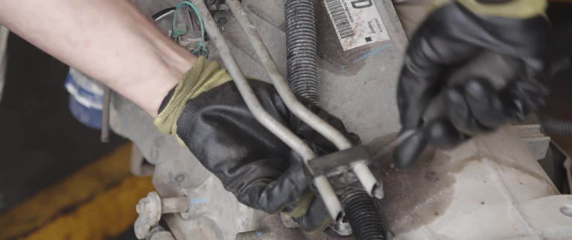 A man is using a screwdriver to remove a piece of metal tubing from an engine block