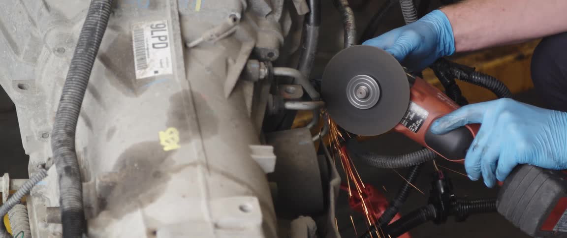 A mechanic uses a grinder to cut a valve off an engine
