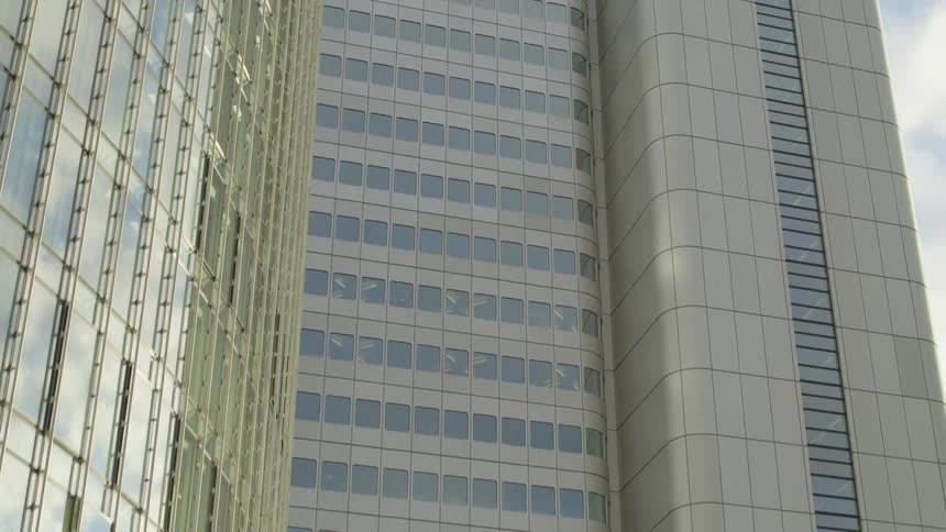 Glass on skyscraper reflects white puffy clouds in blue sky