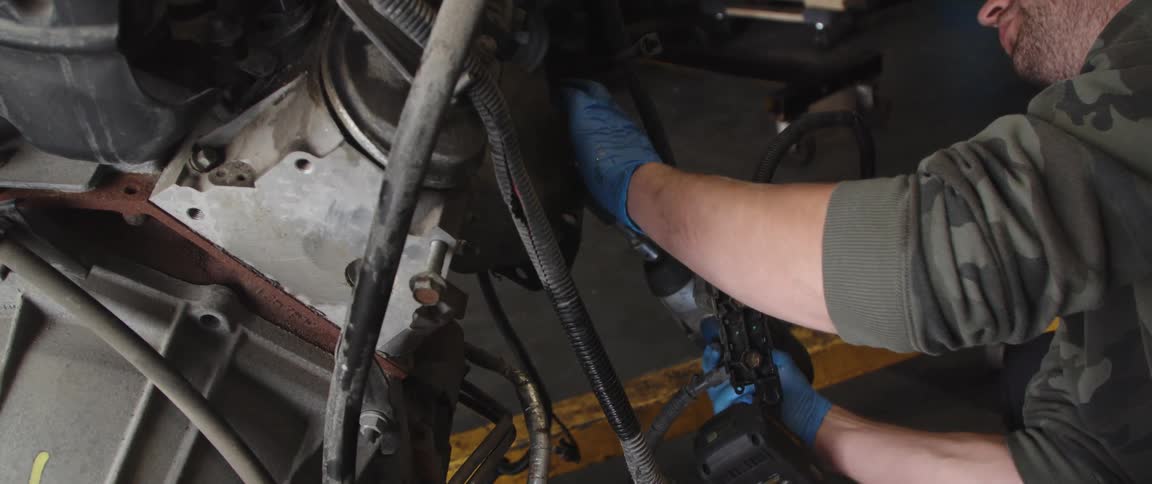 Mechanic works on car engine with power tool