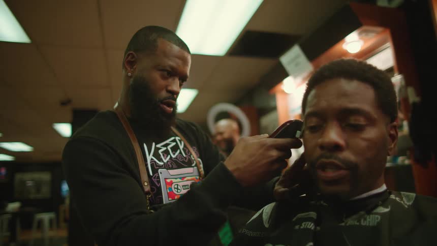 Client sitting in chair talks to barber trimming his hair with electric clippers