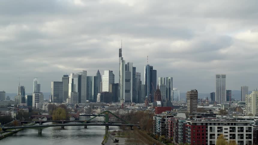 Cars travel across a river on a bridge with a tall city skyline behind