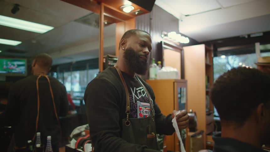 An employee and customers are in a barber shop for hair cuts