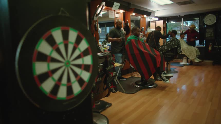 Dart board hanging on the wall of a busy barbershop filled with clients and workers