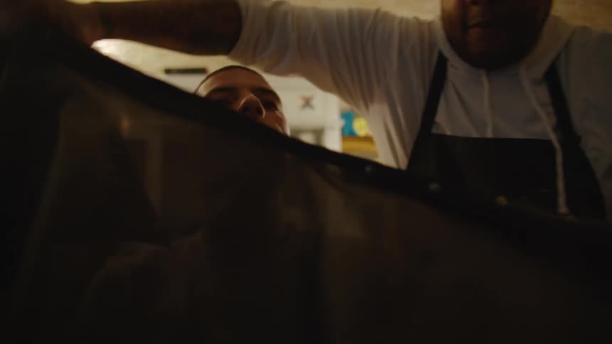 Barber with white shirt and black apron puts apron on customer in barber shop
