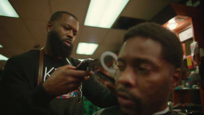 Barber trims mans hair with clippers as client talks