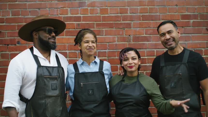 Group of coworkers wearing black aprons dancing and singing in front of a red brick wall