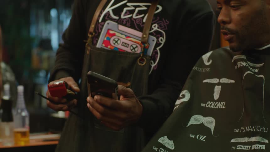 Barber and his customer consult mobile phone as during their discussion