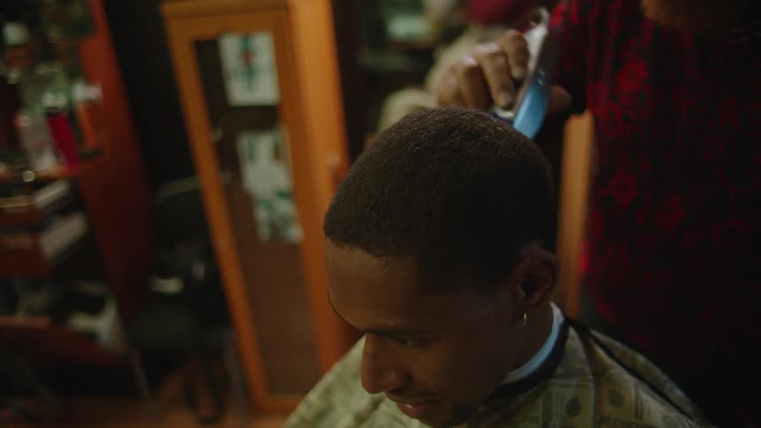 Barber with hat glasses red beard and shirt cuts mans hair with clippers in barbers shop