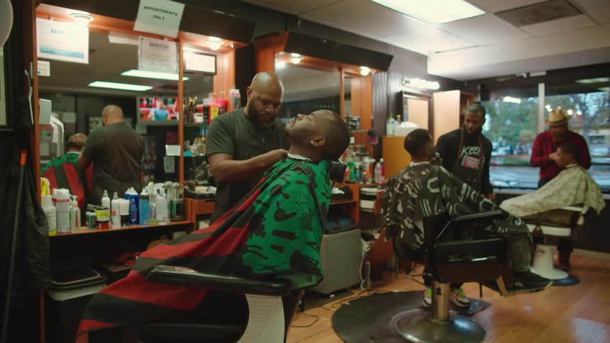 Barbers work on customers sitting in chairs in shop