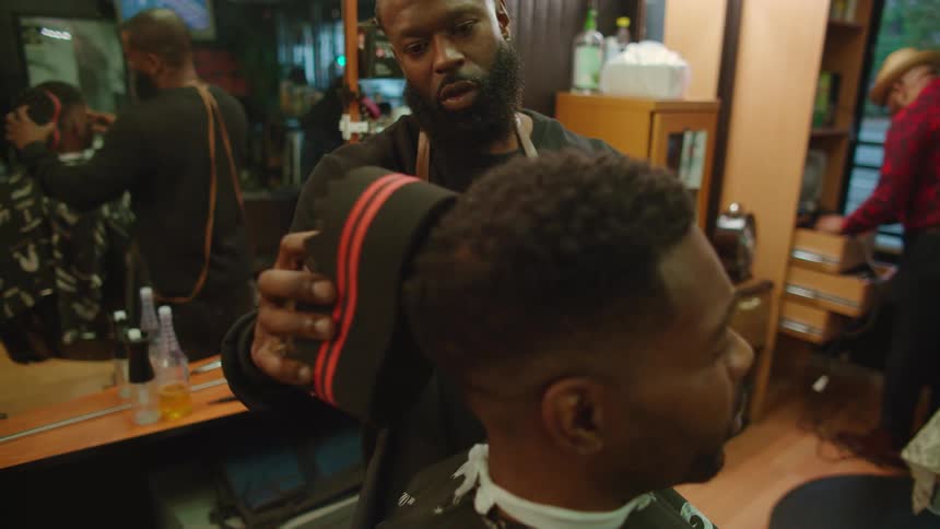 A barber uses a tool to do a seated mans hair